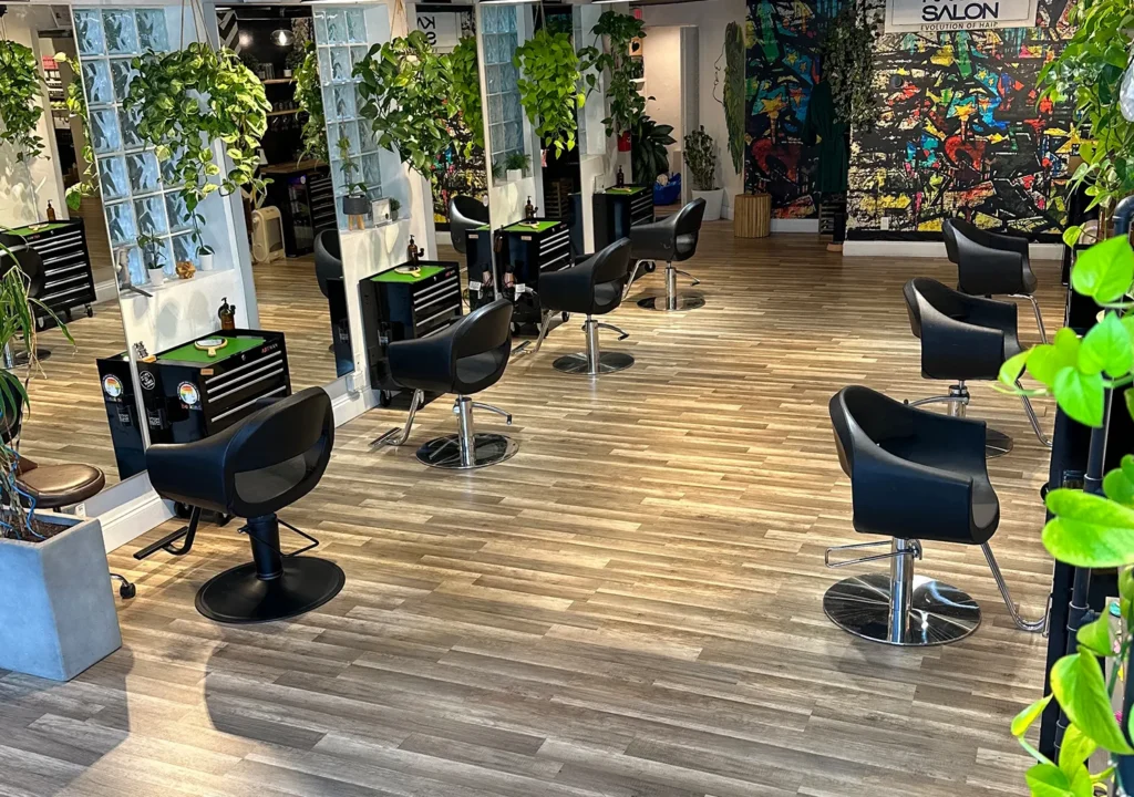 A hair salon interior with rows of black styling chairs for haircuts, workstations, and potted plants against a colorful graffiti-style wall mural. - Ka'ton Salon, Fort Lauderdale FL