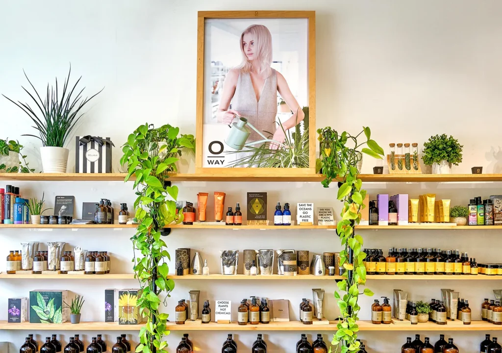 Shelves of hair care products for balayage and haircuts in a shop, with a large poster of a woman using a watering can and trailing green plants. - Ka'ton Salon, Fort Lauderdale FL
